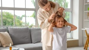 Mother carefully parting her young daughter's hair to inspect the scalp for lice bite marks during an at-home head check