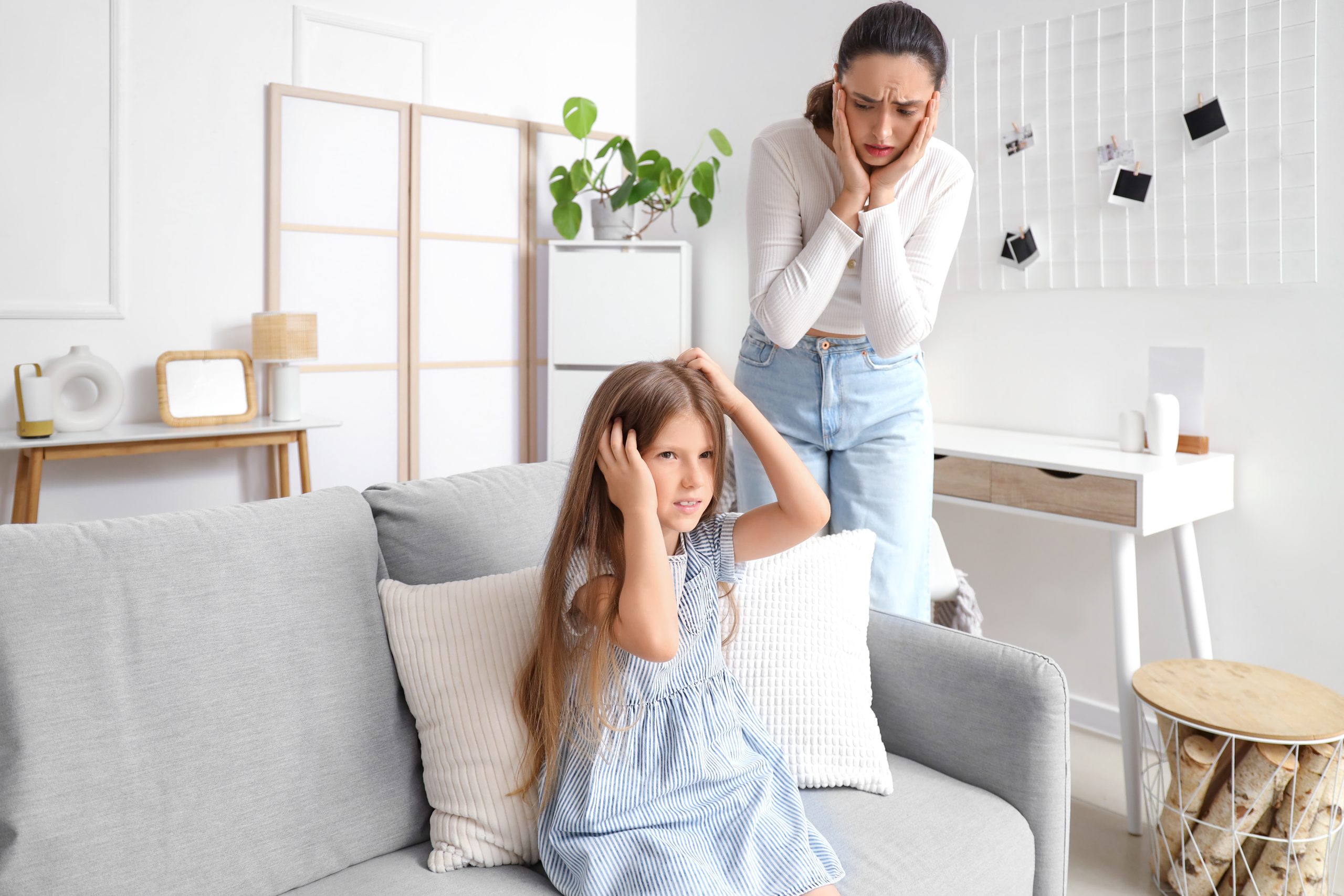 Worried mother watching her young daughter scratch her itchy head at home