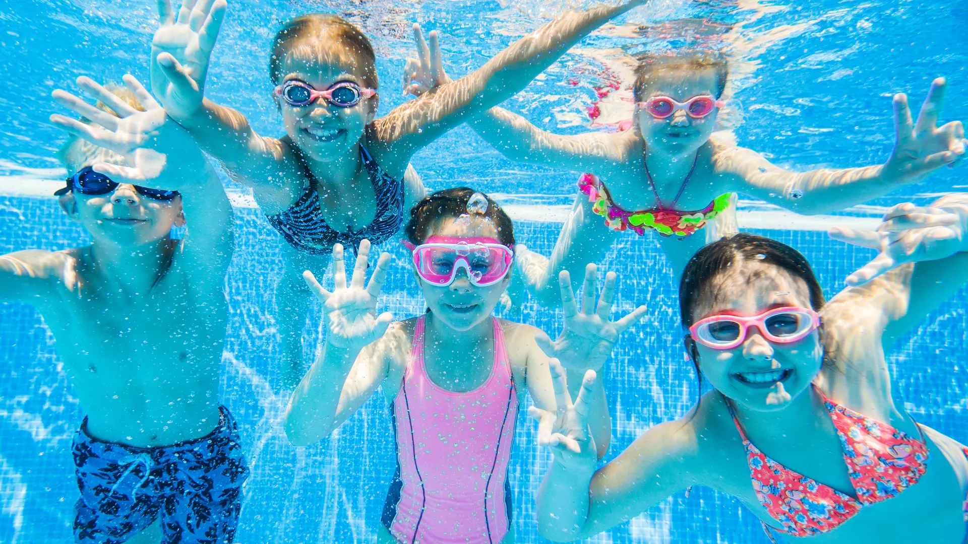 Children swimming underwater in a clear blue pool