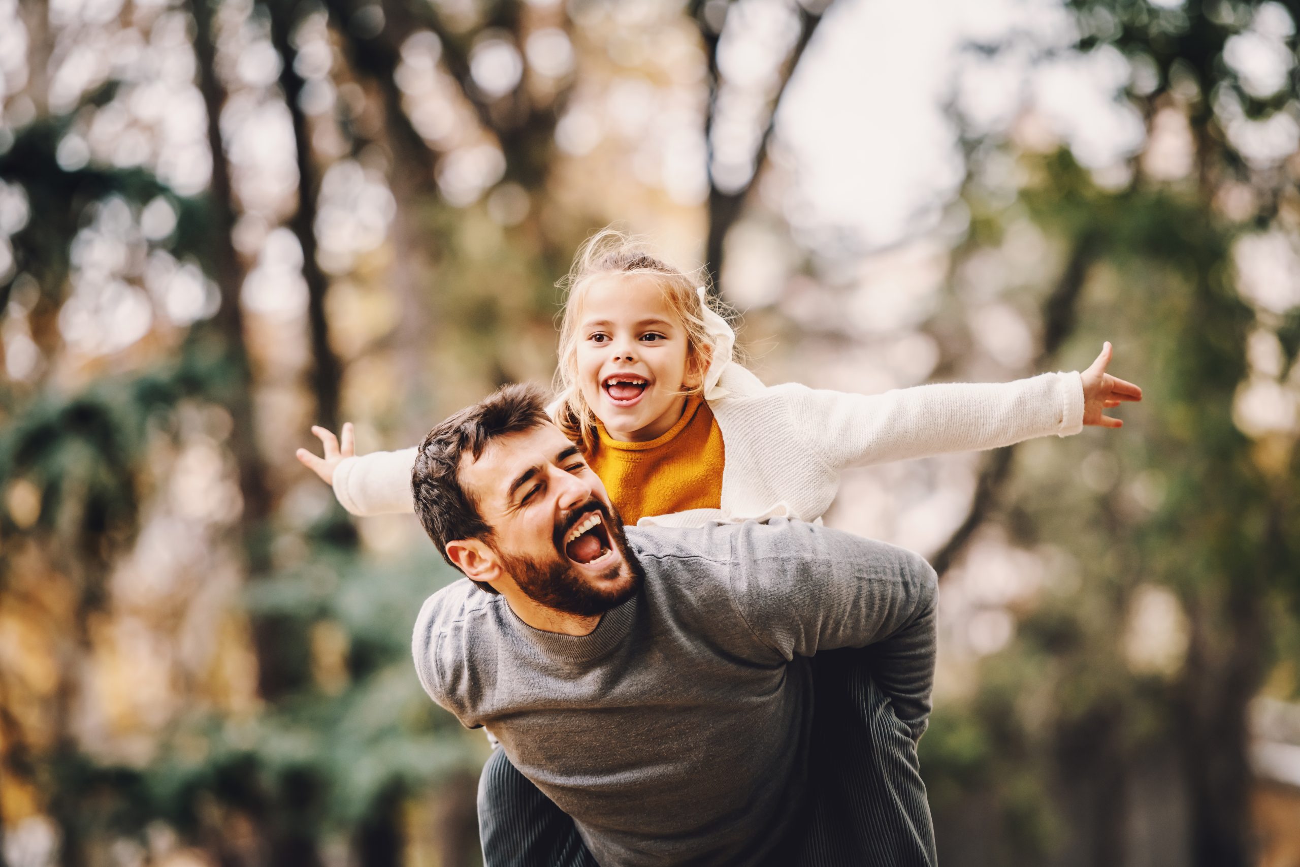 Bearded father carrying his laughing young daughter on his back outdoors in autumn