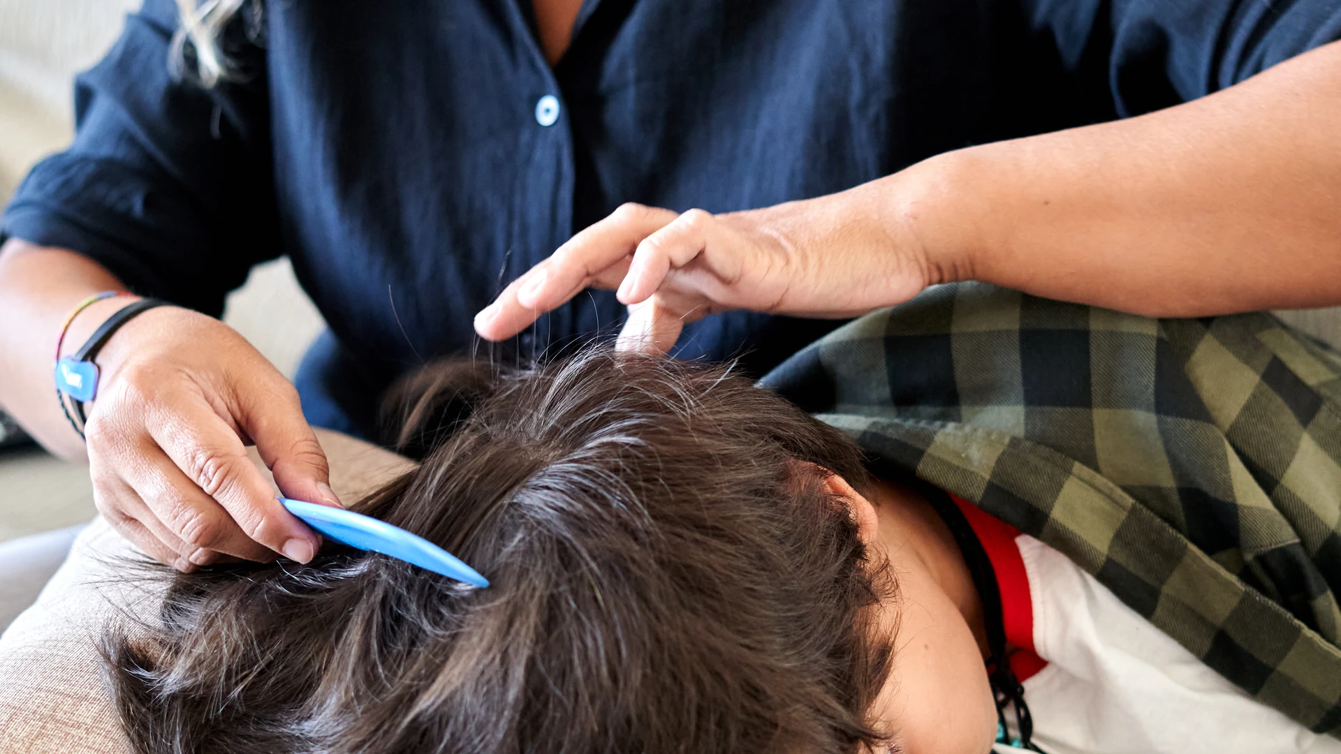 Hands parting a resting person's dark hair with a blue comb.