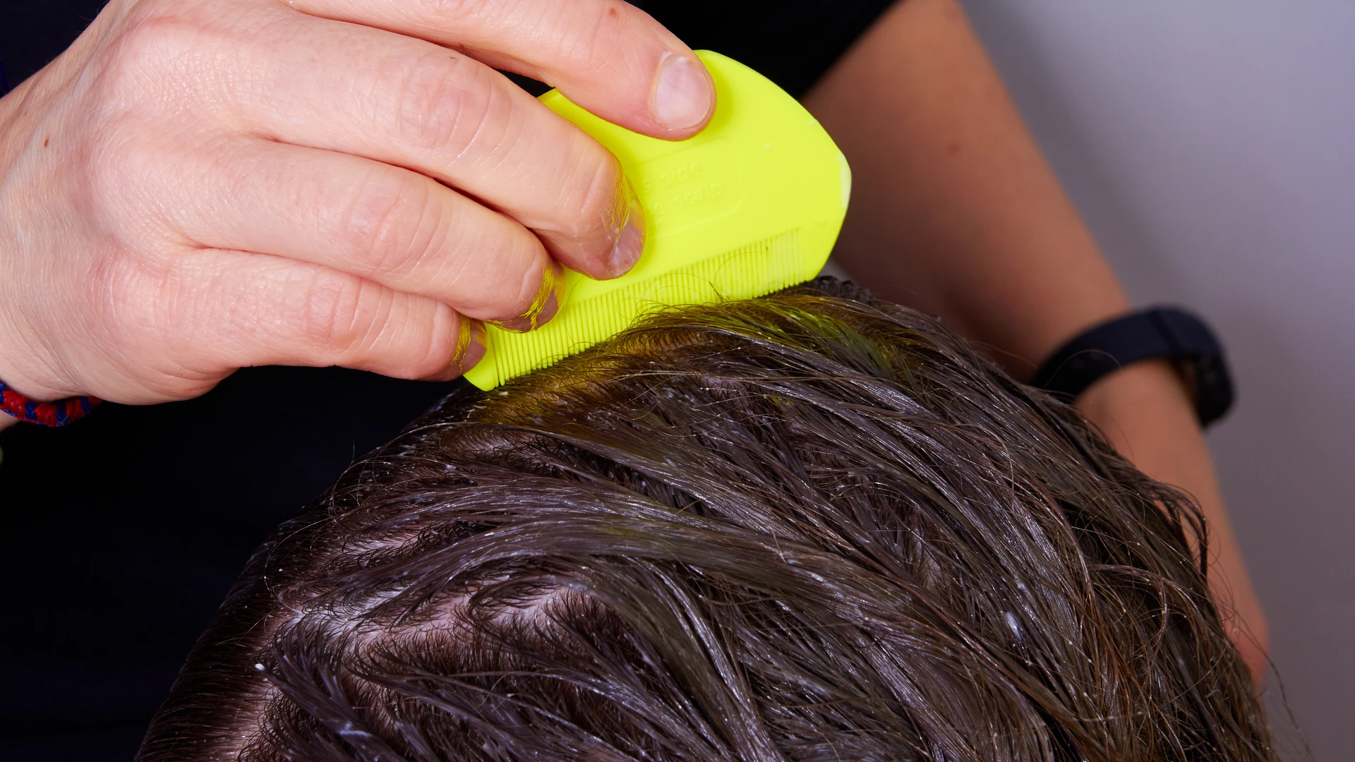 A bright yellow-green fine-tooth comb passing through wet brown hair.