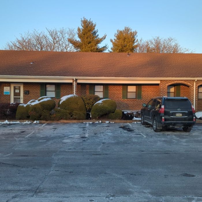 Treatment image by Lice Lifters Of Bucks County - Lice Treatment and Lice Removal Single-story brick building beside a parking lot with a parked vehicle and patches of snow.