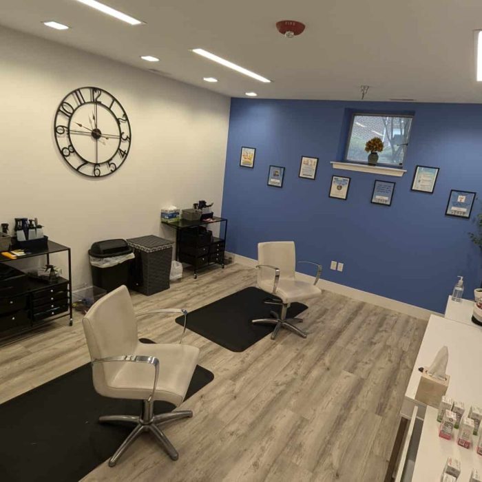 Treatment image by Lice Lifters Of Bucks County - Lice Treatment and Lice Removal Reclining chairs on black floor mats beneath a wall clock and framed items.